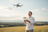Man operating a drone in an open field with a clear sky